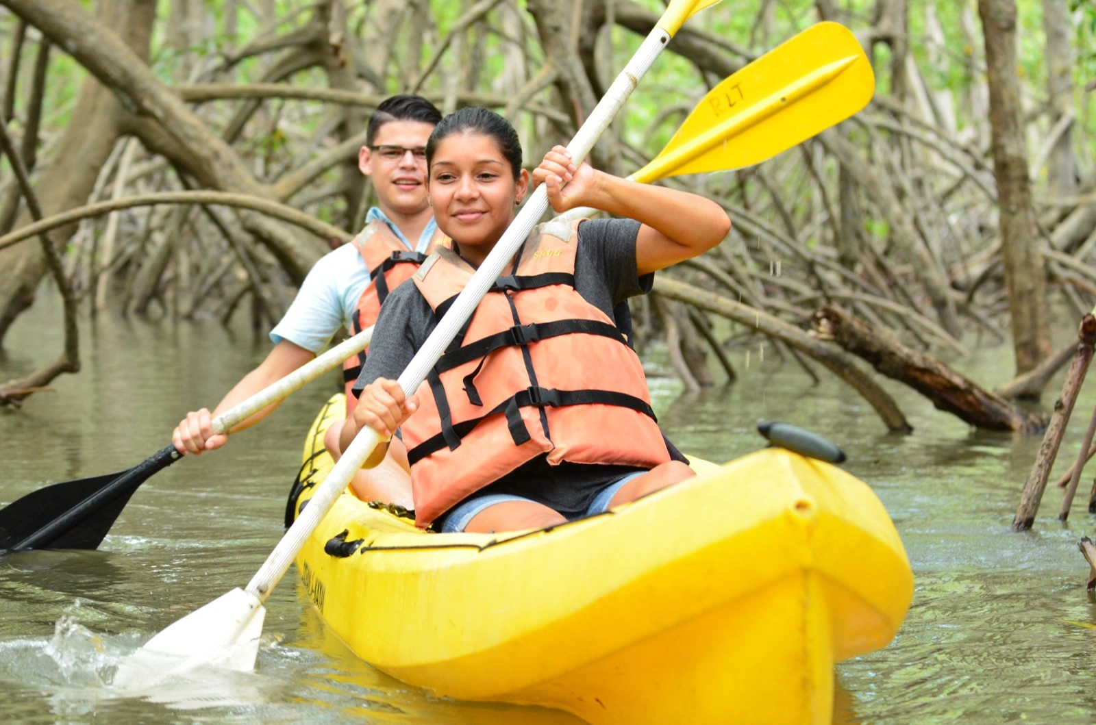 Two guests paddling a yellow kayak through the arching mangrove roots at the Isla Damas estuary near Manuel Antonio, Costa Rica